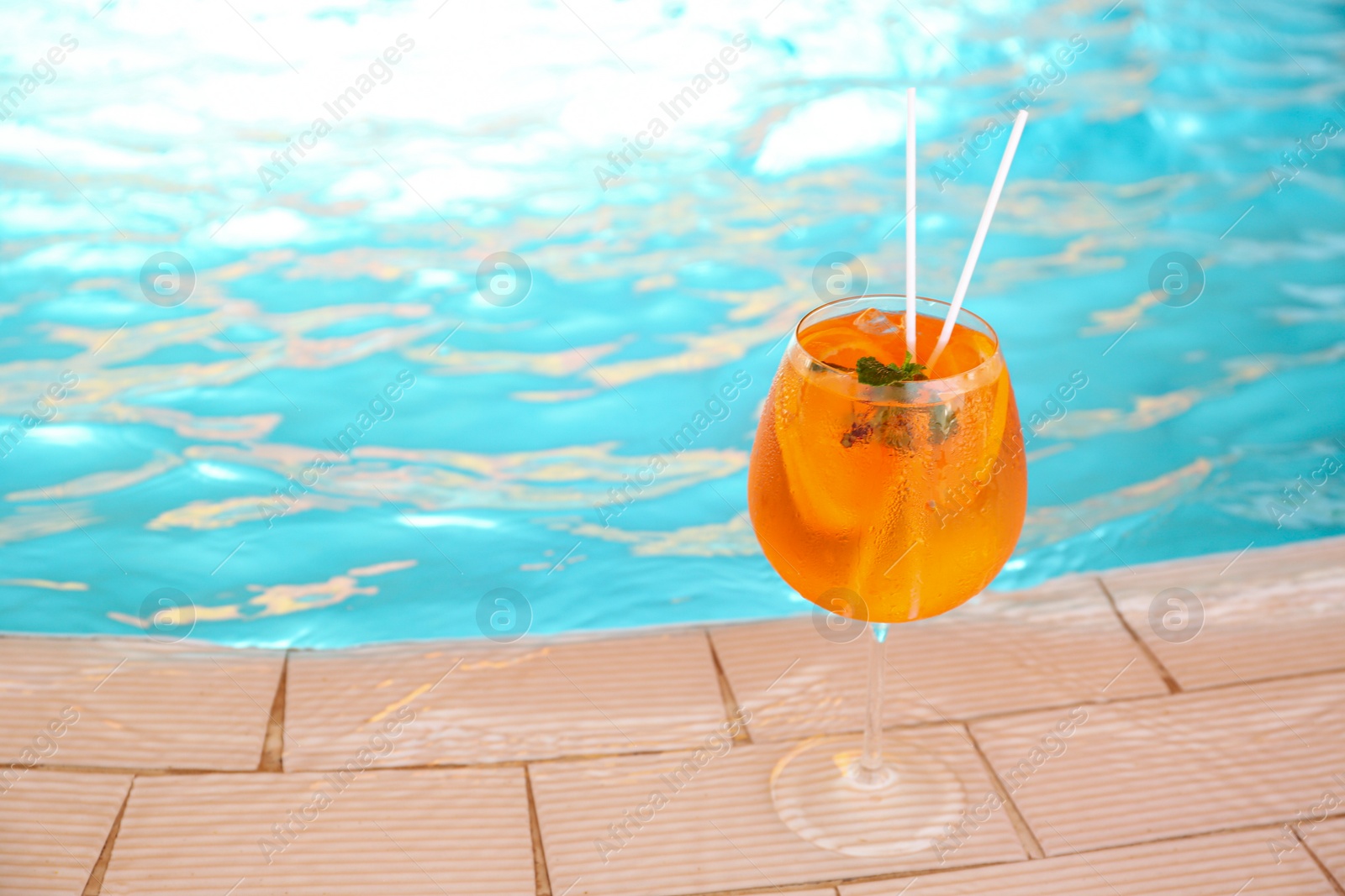 Photo of Glass of delicious cocktail near swimming pool, space for text. Refreshing drink