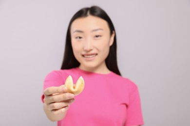 Photo of Asian woman against grey background, focus on tasty fortune cookie with prediction