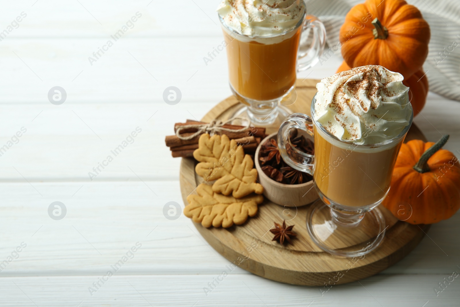 Photo of Tasty pumpkin latte with whipped cream in glasses, spices and cookies on white wooden table. Space for text