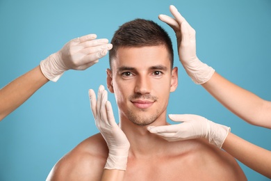 Photo of Doctors examining man's face for cosmetic surgery on light blue background