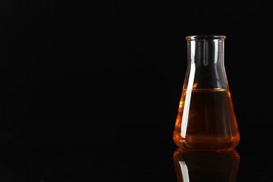 Photo of Glass flask with yellow oil on black background, space for text