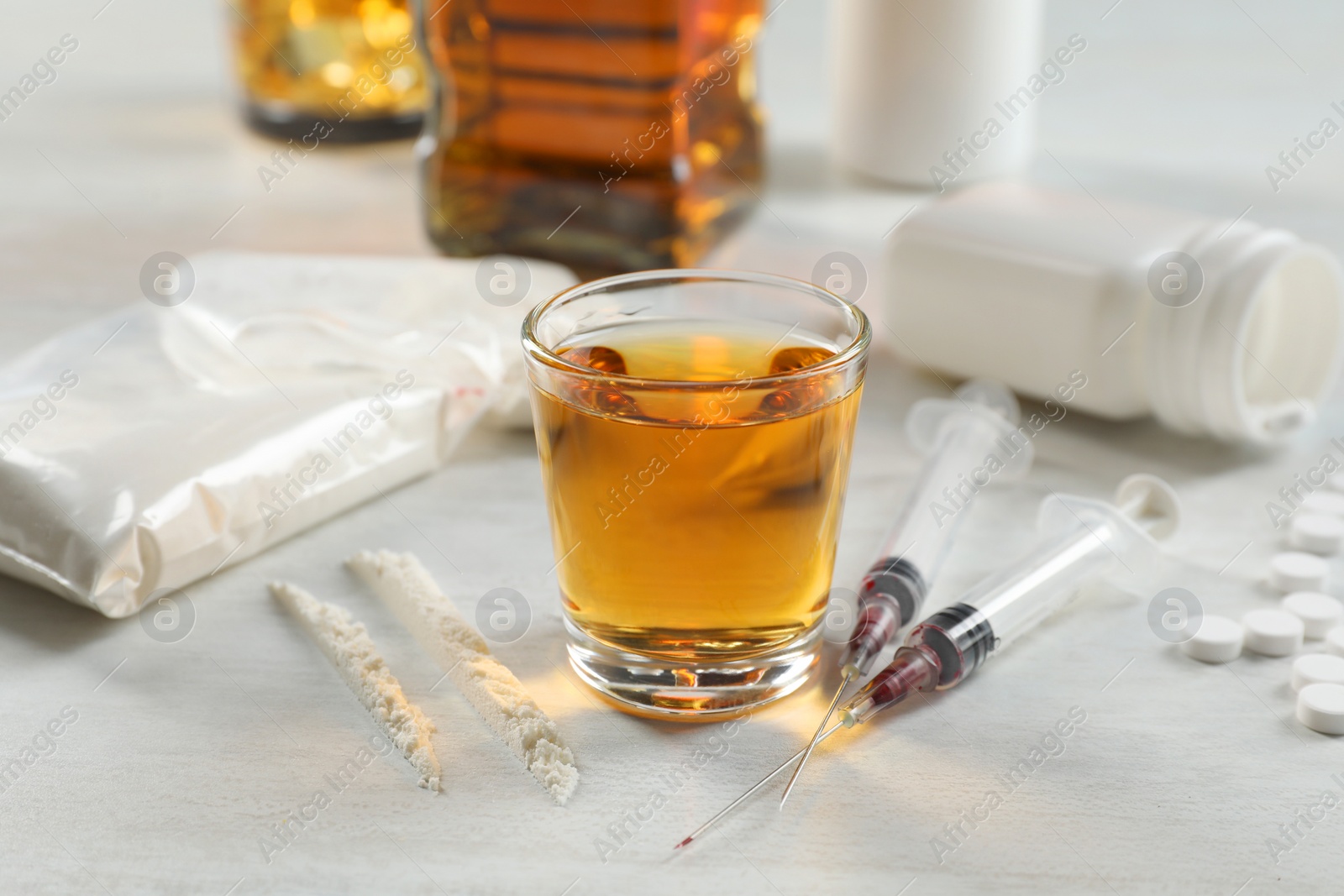 Photo of Alcohol and drug addiction. Whiskey in glass, syringes, cocaine and pills on white table