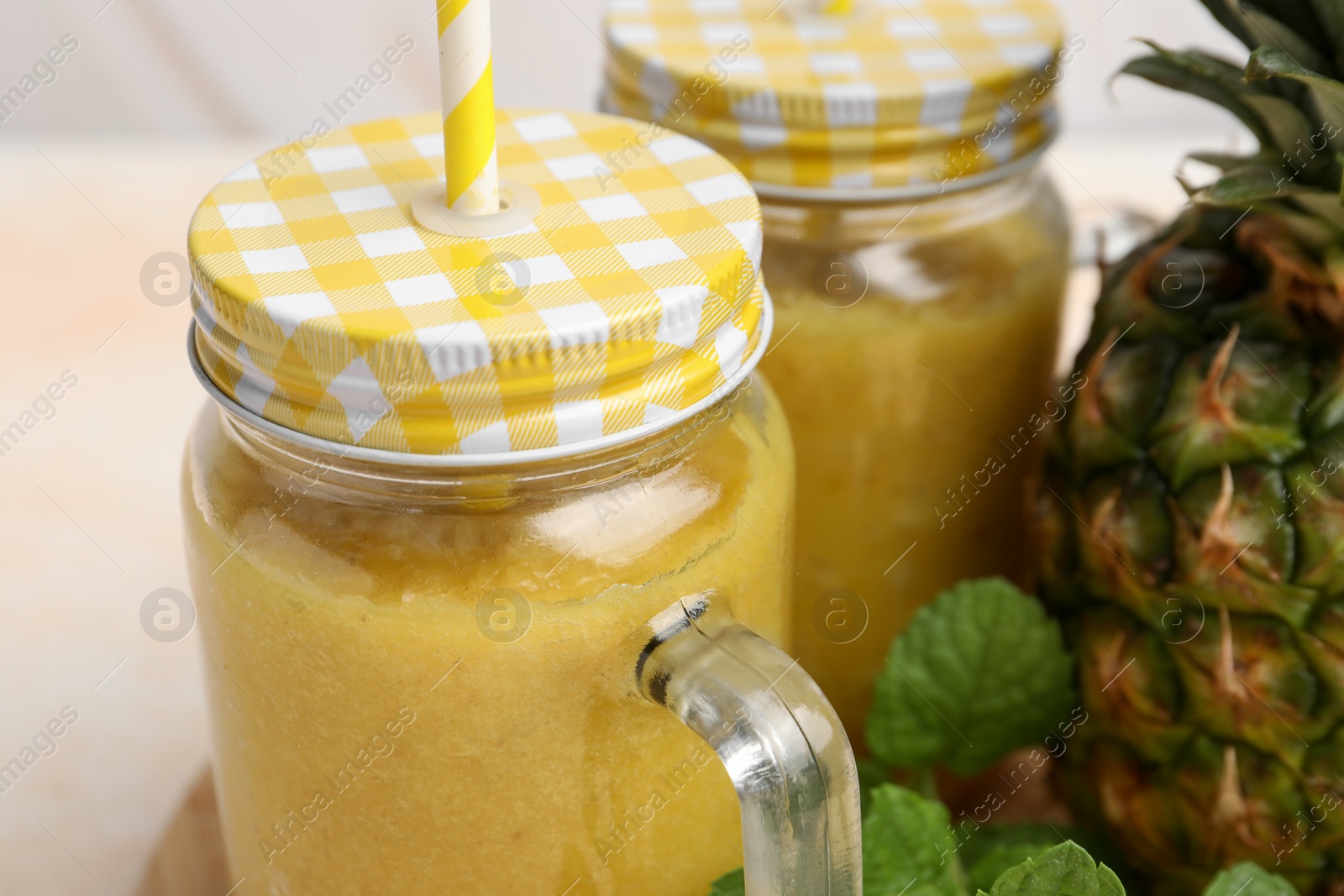 Photo of Tasty pineapple smoothie in mason jars and fruit on table, closeup