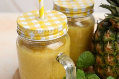 Tasty pineapple smoothie in mason jars and fruit on table, closeup