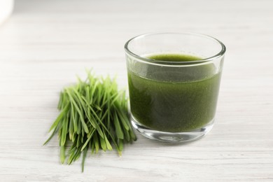 Photo of Wheat grass drink in glass and fresh sprouts on white wooden table, closeup