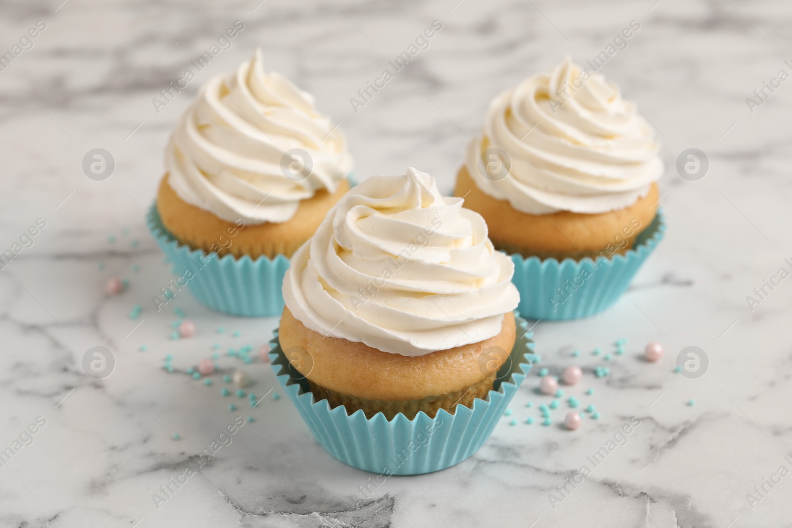 Photo of Delicious cupcakes decorated with cream on white marble table