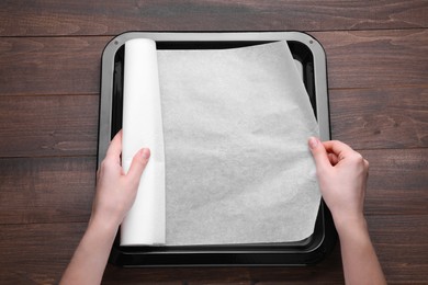 Photo of Woman putting parchment paper into baking pan over wooden table, top view. Space for text