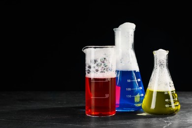 Photo of Laboratory glassware with colorful liquids on dark table against black background, space for text. Chemical reaction