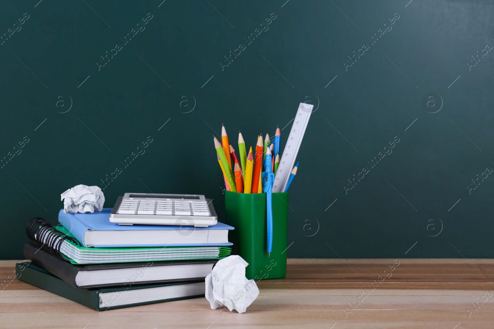 Photo of Set of stationery and crumpled paper on wooden table near chalkboard. Doing homework