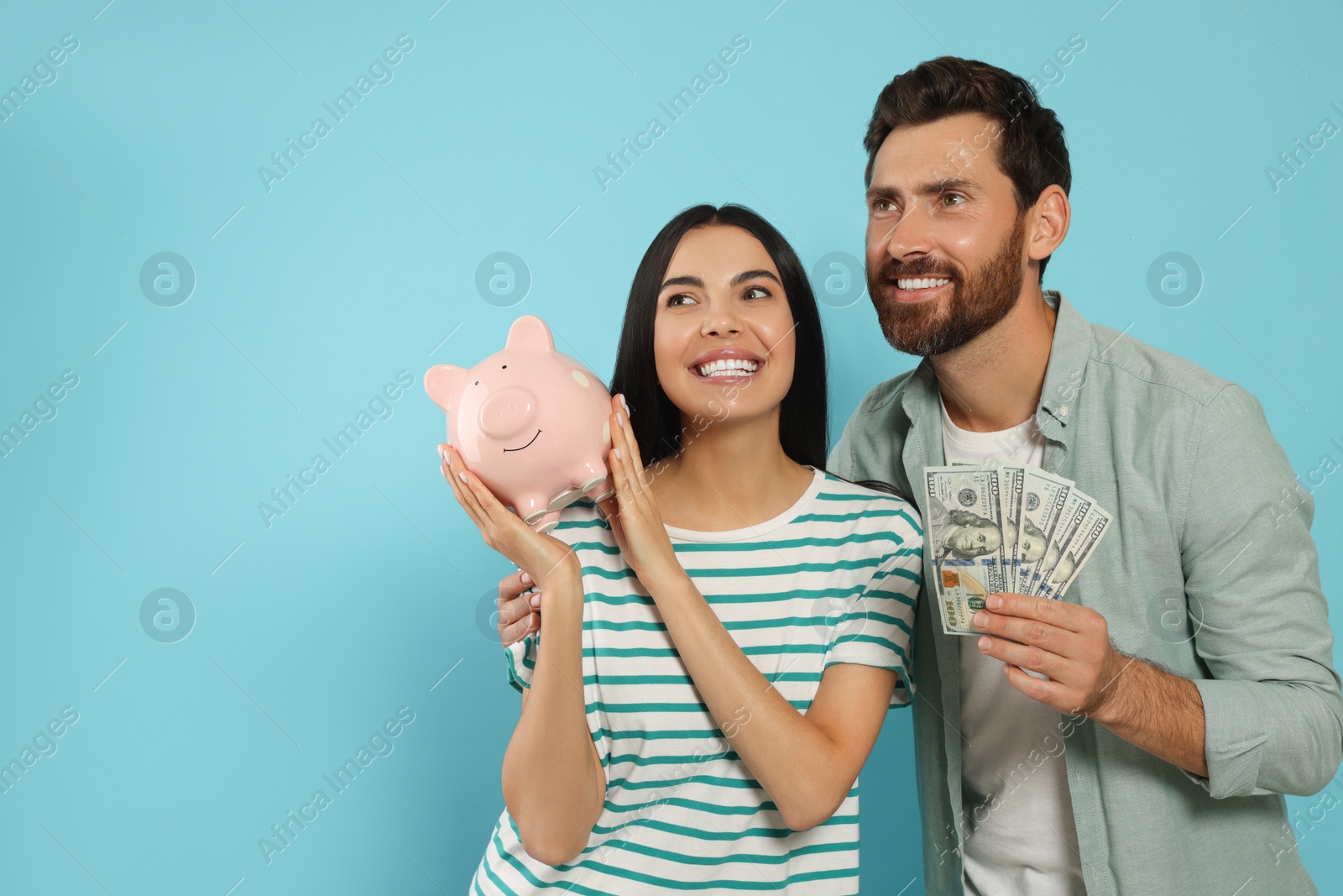 Photo of Happy couple with money and ceramic piggy bank on light blue background, space for text