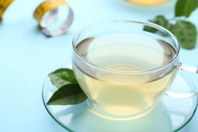 Photo of Glass cup of diet herbal tea and green leaves on light blue background, closeup