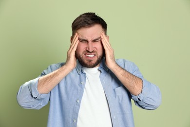 Man suffering from migraine on light green background