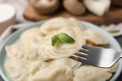 Photo of Delicious dumpling (varenyk) with basil leaf on fork over plate, closeup