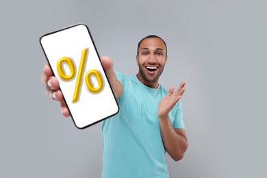 Image of Discount, offer, sale. Emotional man showing mobile phone with percent sign on screen, grey background