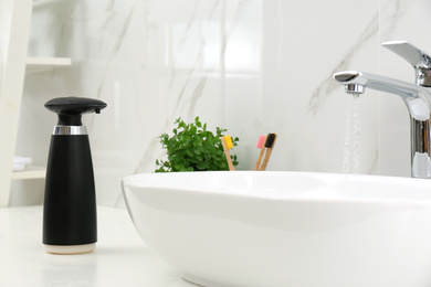 Photo of Modern automatic soap dispenser near sink in bathroom, closeup