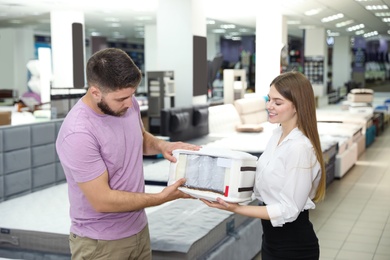 Photo of Young saleswoman showing sample of modern orthopedic mattress to customer in store