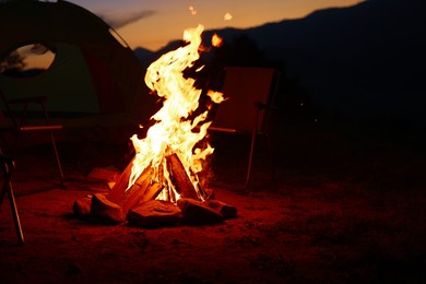 Photo of Beautiful bonfire and folding chairs near camping tent outdoors in evening