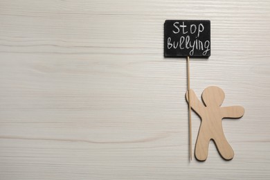 Photo of Human figure holding chalkboard with phrase Stop Bullying on white wooden table, flat lay. Space for text