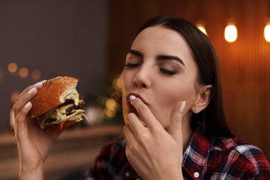 Photo of Young woman eating tasty burger in cafe
