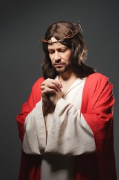 Photo of Jesus Christ with crown of thorns praying on grey background