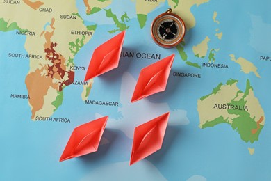 Bright paper boats and compass on world map, flat lay