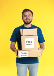 Photo of Male courier holding parcels with stickers Free Delivery on yellow background
