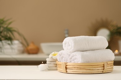 Photo of Spa composition. Rolled towels, massage stones, burning candle and plumeria flower on table. Space for text
