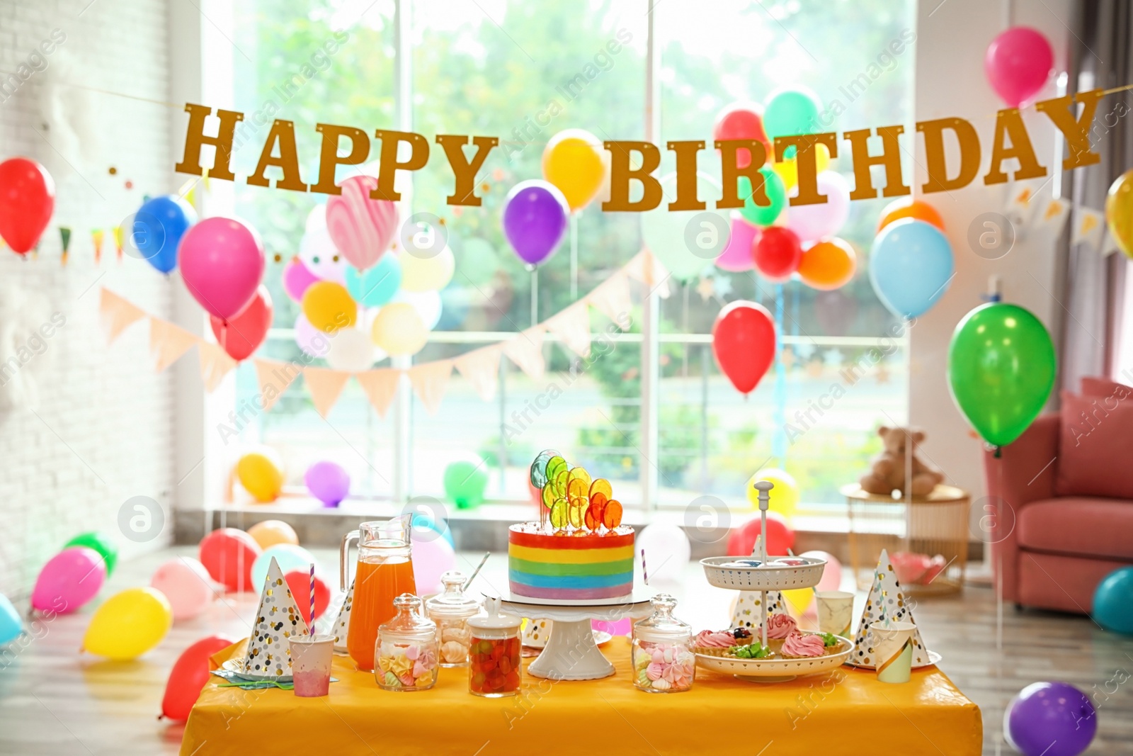 Photo of Bright birthday cake and other treats on table in decorated room