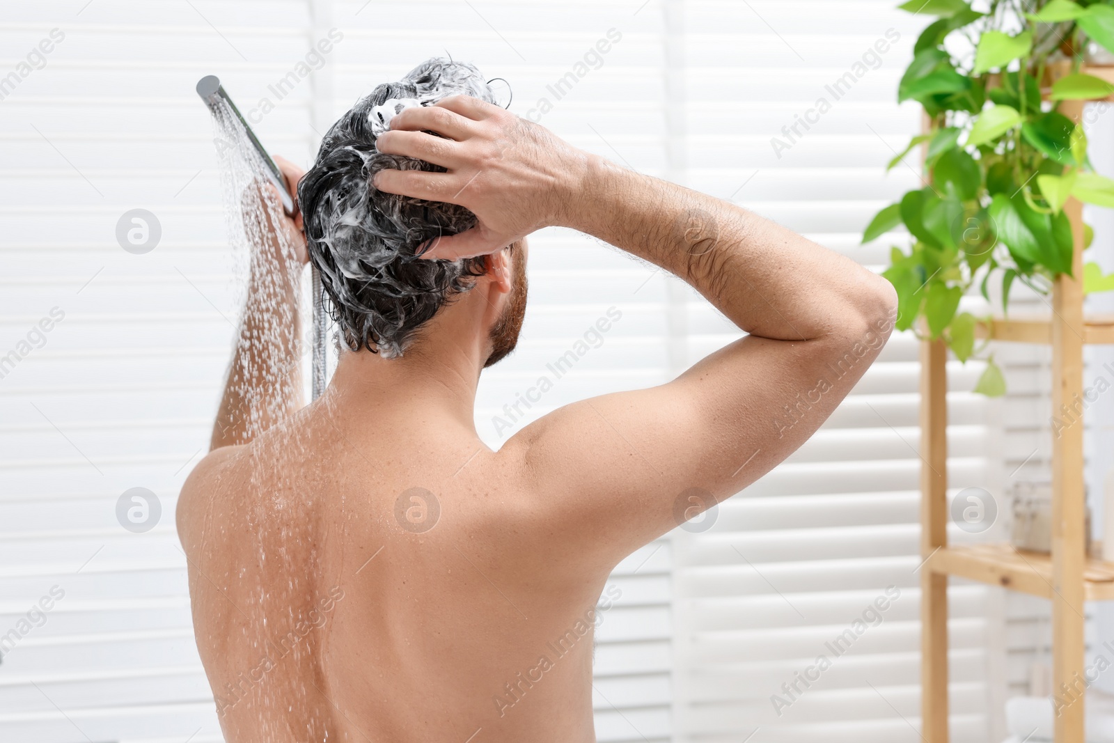 Photo of Man washing his hair with shampoo in bathroom, back view