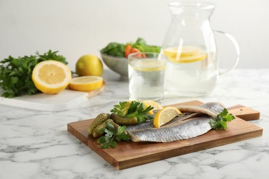Salted herring fillets served with pickles, parsley and lemon on white marble table