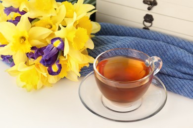 Photo of Cup of aromatic tea, beautiful yellow daffodil and iris flowers on white table