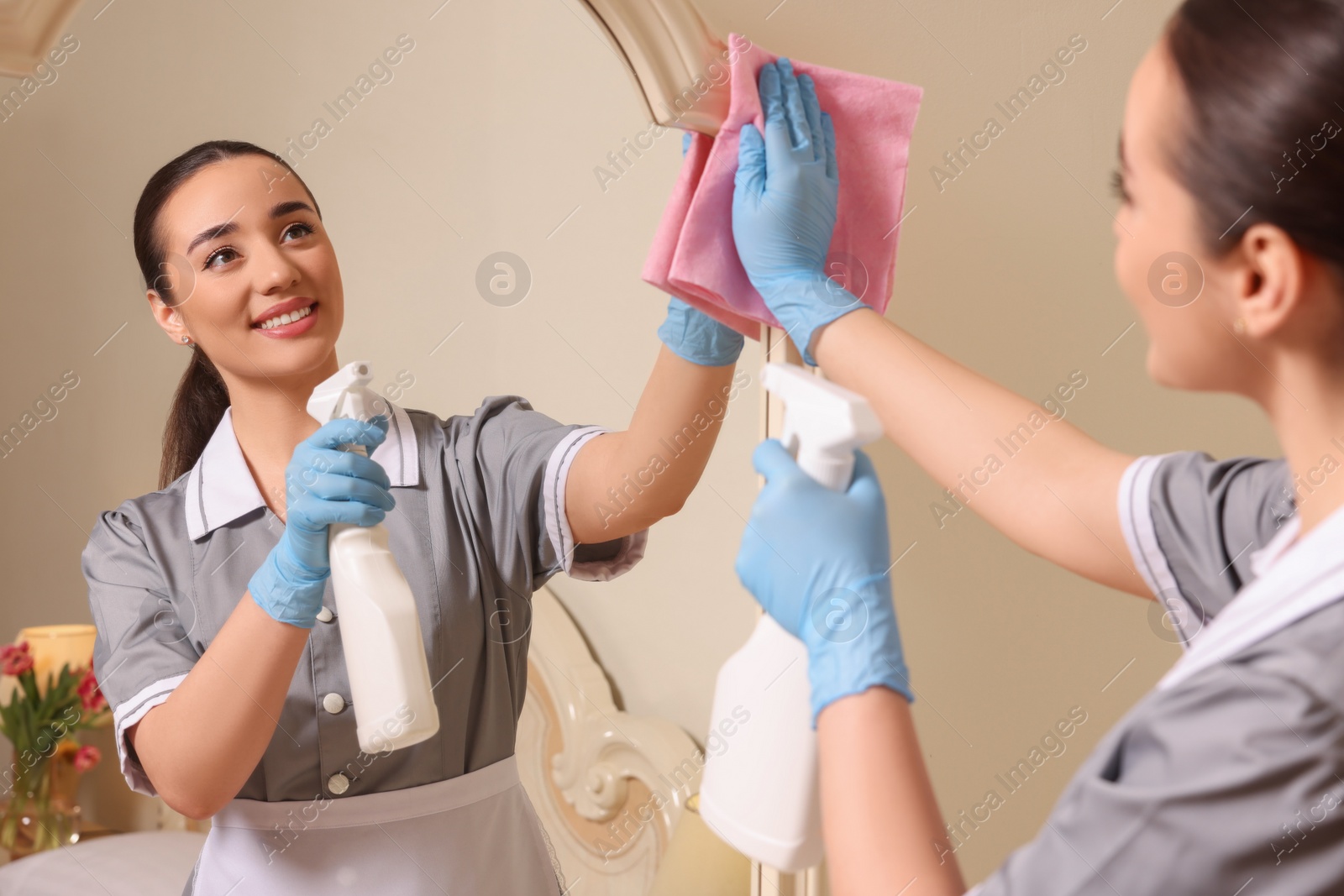 Photo of Young chambermaid cleaning mirror in hotel room