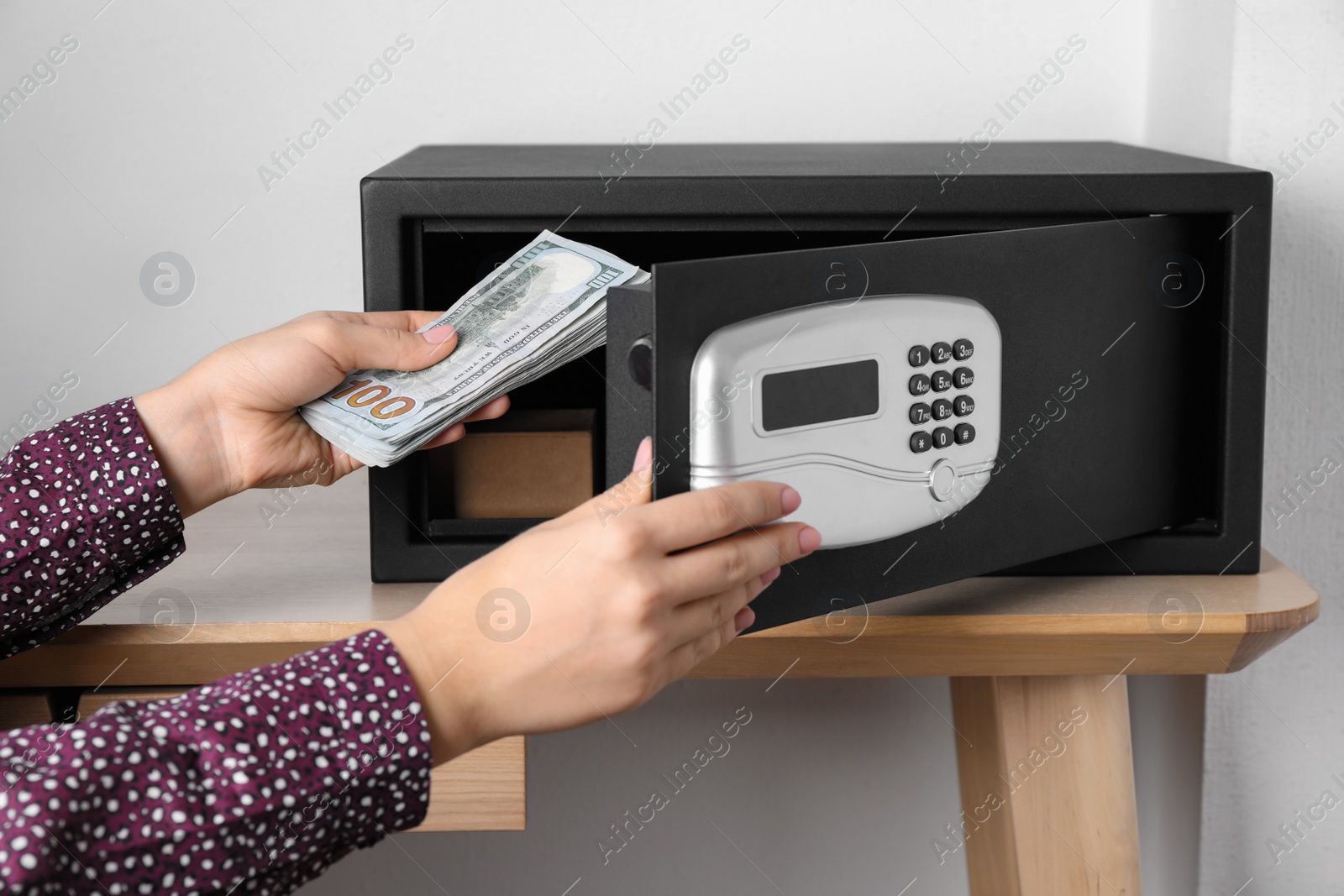 Photo of Woman putting money into steel safe with electronic lock, closeup