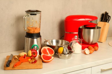 Photo of Modern red stand mixer, blender and different ingredients on white marble countertop in kitchen