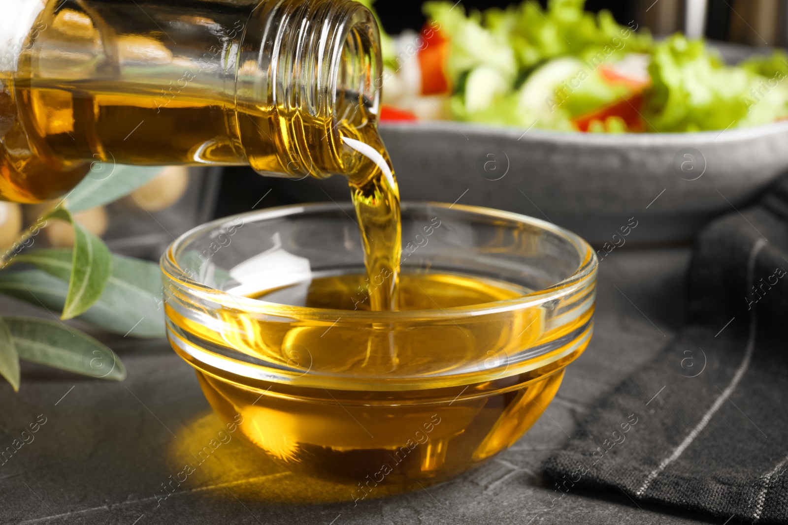 Photo of Pouring cooking oil into bowl on grey table, closeup