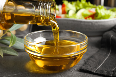 Photo of Pouring cooking oil into bowl on grey table, closeup