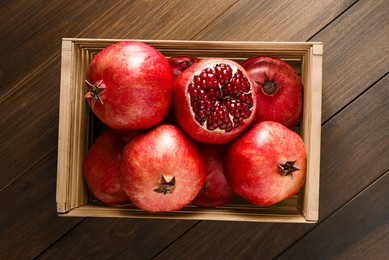 Photo of Ripe pomegranates in crate on wooden table, top view