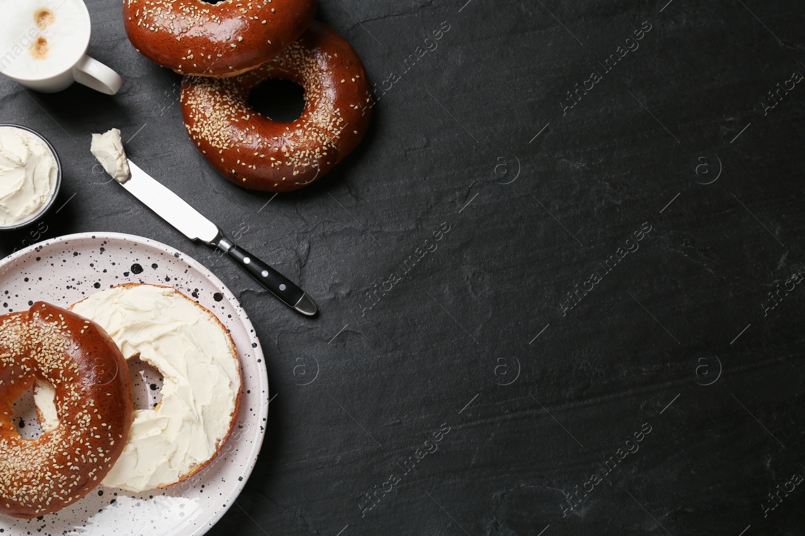 Photo of Delicious bagel with cream cheese and coffee on black table, flat lay. Space for text