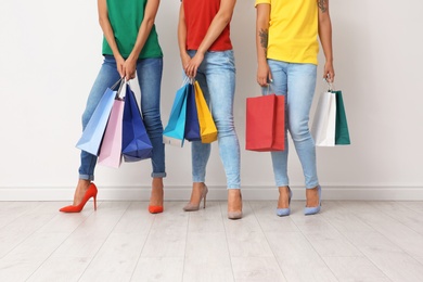 Photo of Group of young women with shopping bags near light wall