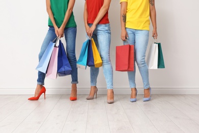 Group of young women with shopping bags near light wall