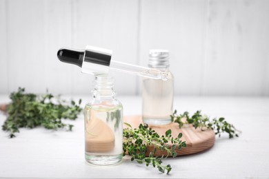 Photo of Thyme essential oil and fresh plant on white wooden table