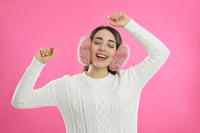 Photo of Beautiful young woman wearing earmuffs on pink background