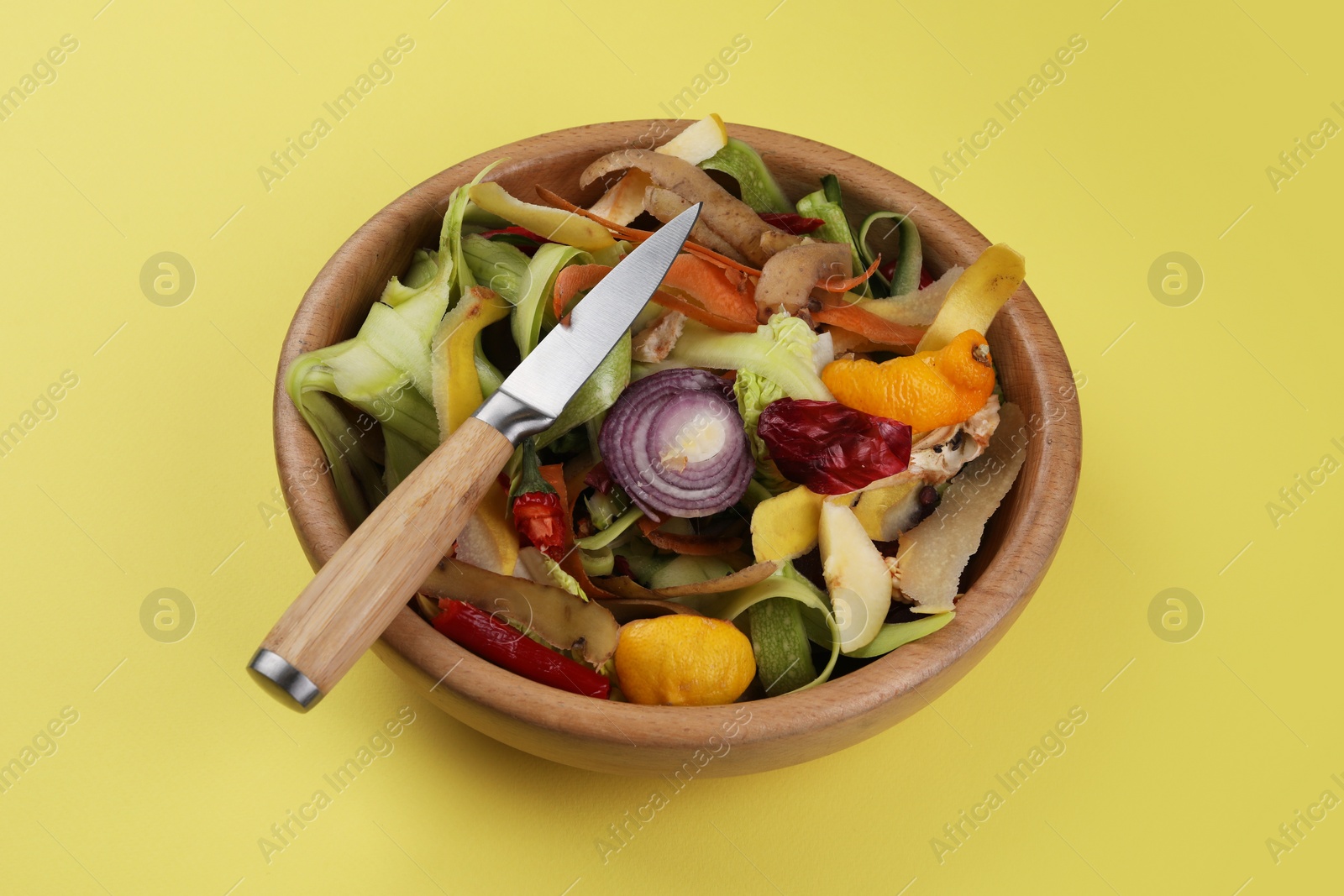 Photo of Peels of fresh vegetables and knife on yellow background