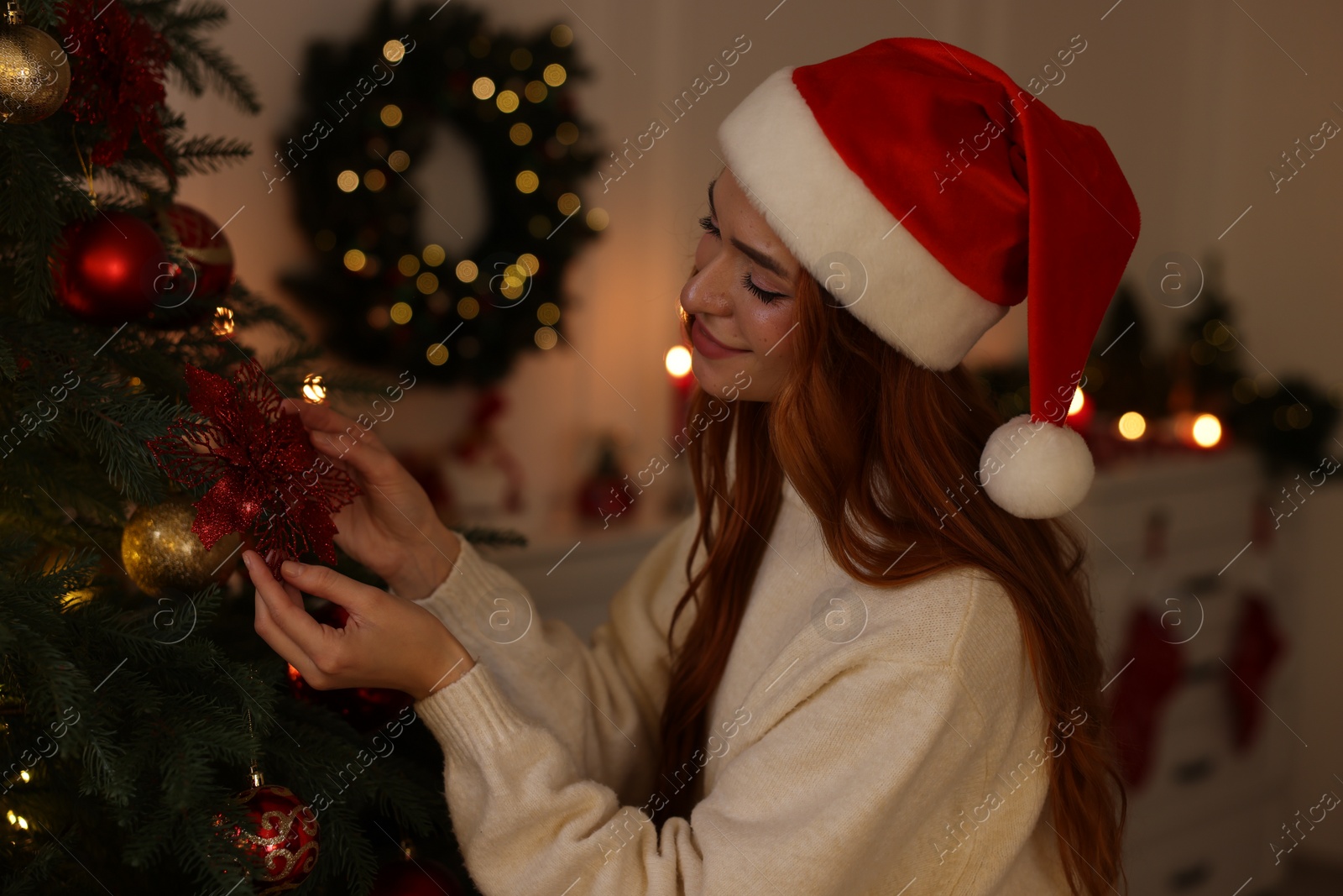 Photo of Beautiful young woman in Santa hat decorating Christmas tree at home