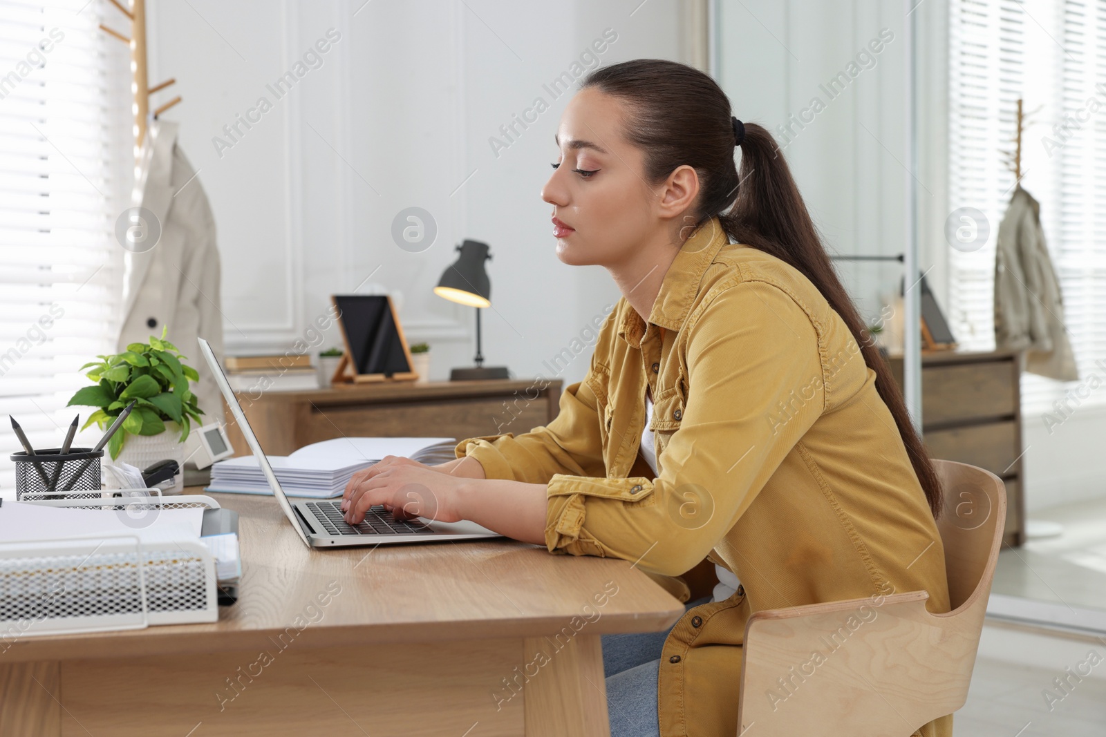 Photo of Young woman with poor posture using laptop at table indoors