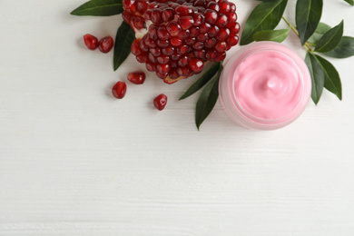 Jar with natural facial mask, pomegranate seeds and green leaves on white wooden table, flat lay. Space for text