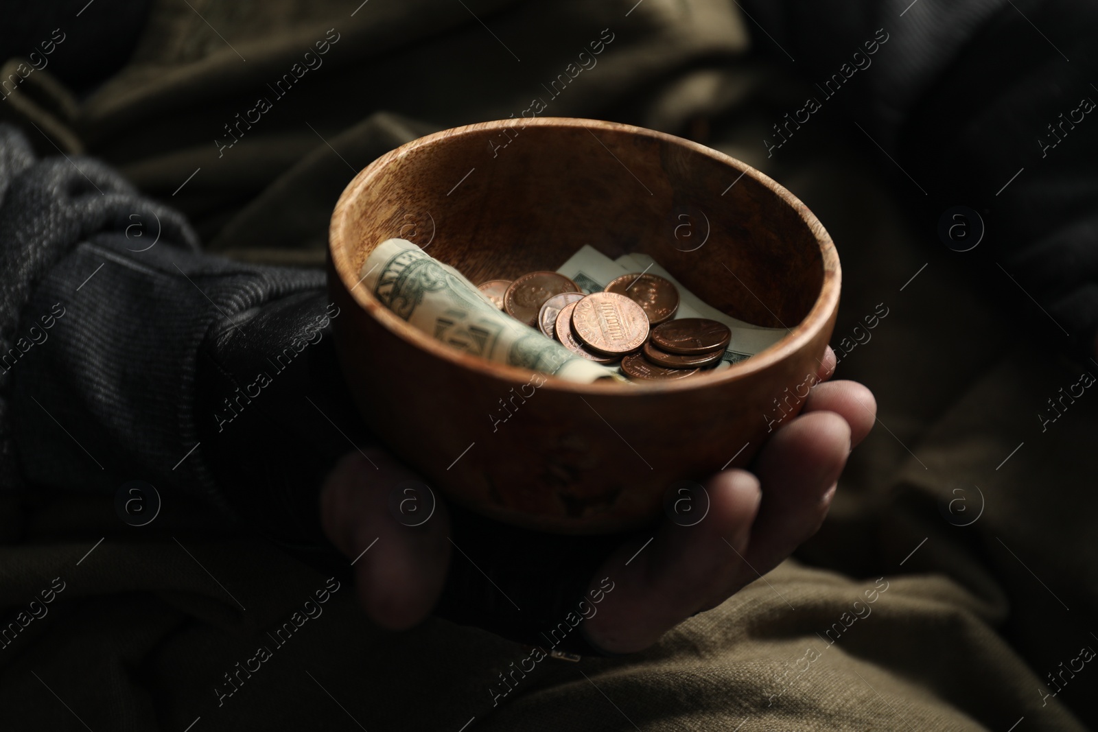 Photo of Poor homeless man holding bowl with donations on blurred background, closeup