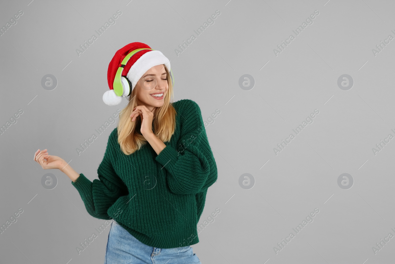 Photo of Happy woman with headphones on grey background, space for text. Christmas music