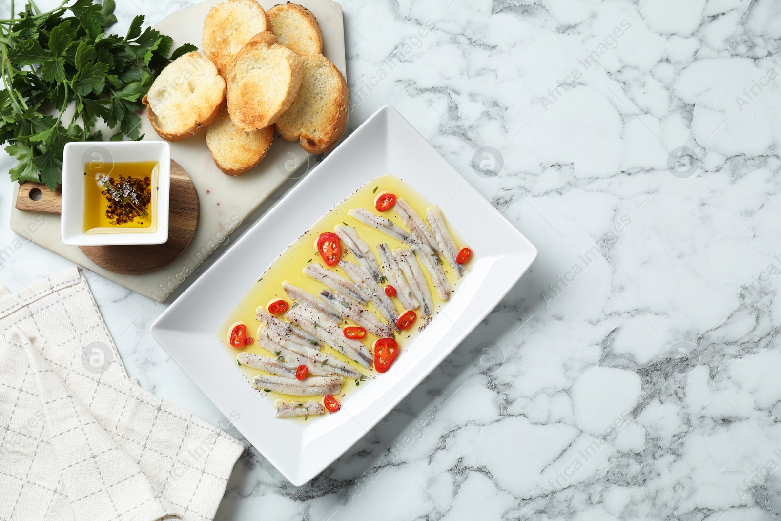 Photo of Tasty pickled anchovies with spices and products on white marble table, flat lay. Space for text