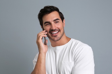 Photo of Handsome young man talking on smartphone against grey background